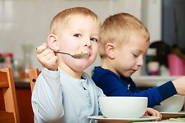 Två små barn sitter vid ett bord och äter.