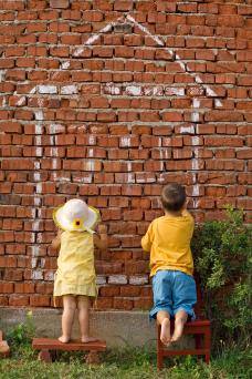 Foto visar två barn som ritar hus på en röd tegelvägg